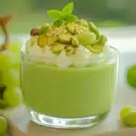 A creamy bowl of pistachio pudding garnished with grapes and nuts.